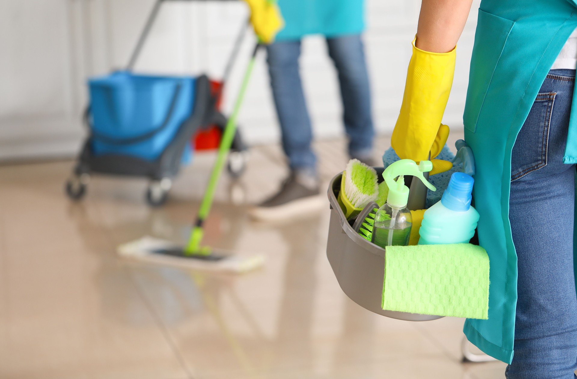 Hand in yellow glove holding a caddy with cleaning supplies with blurred background